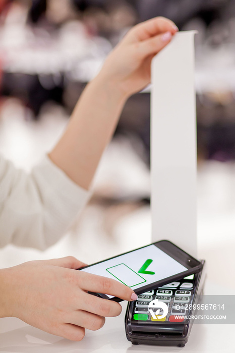 Customer paying bill through smartphone using NFC technology. Closeup of hand making payment through contactless machine.Woman hand holding mobile phone paying the bill with contact less technology.