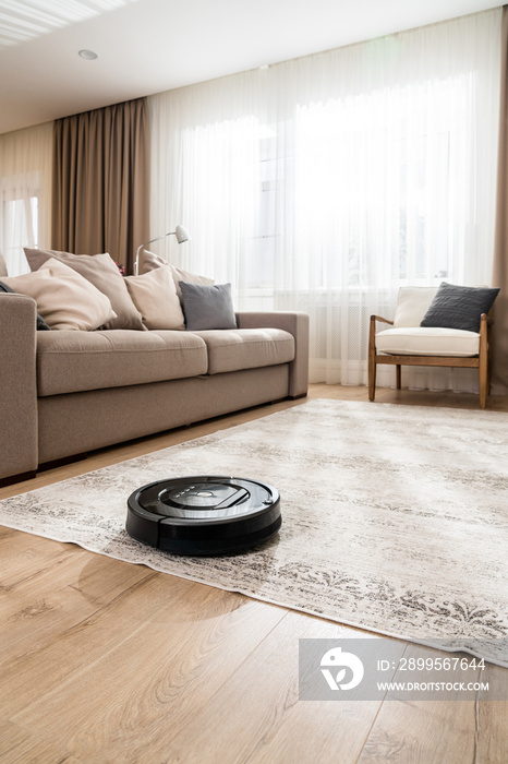 Vertical shot of a black robotic vacuum cleaner in a new living room in light beige and gray tones