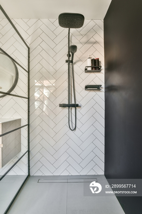 Shower faucets attached to tiled wall near glass partition and ornamental curtail in washroom at home