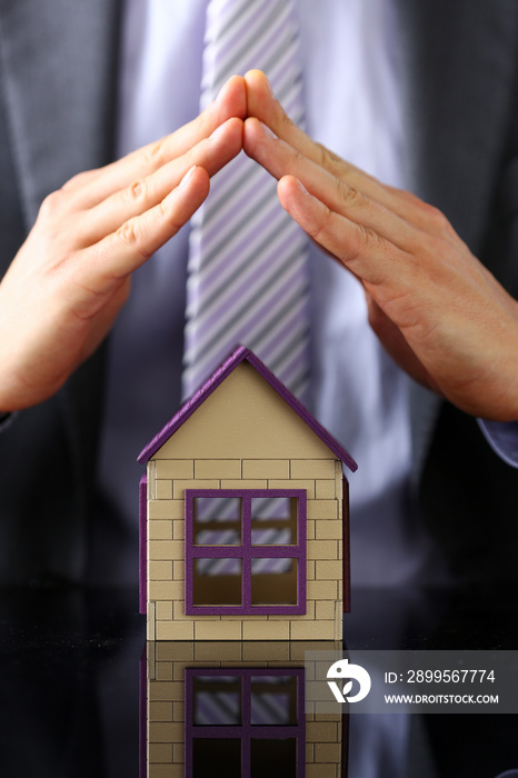 Man in suit and tie cover with arms little toy house closeup. Palm shelter, save and trust, owner wealth, sell or rental structure, loan idea, no problems, buy future plan concept