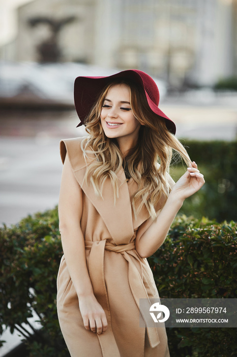 Outdoor portrait of a young beautiful woman with long platinum blond hair in modish outfit. Model girl in stylish coat and trendy hat. Female fashion, beauty concept