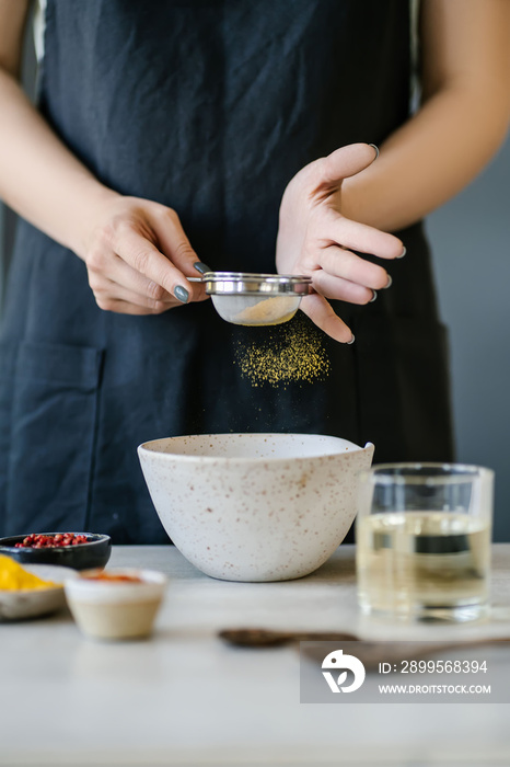 The girl sifts turmeric into a bowl.