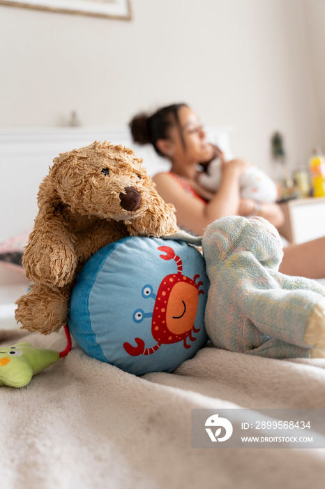 Toys lying on bed in front of mother carrying newborn baby girl in bedroom