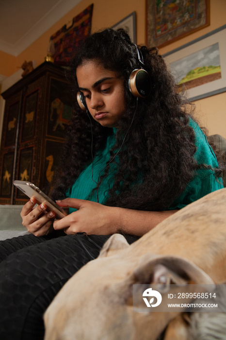 Curvy Indian girl with Cerebral Palsy wearing headphones next to her dog in the living room