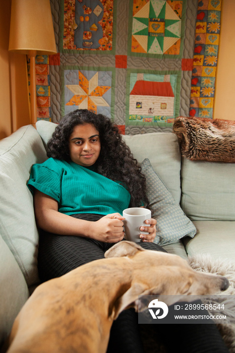 Curvy Indian girl with Cerebral Palsy drinking coffee next to her dog in the living room