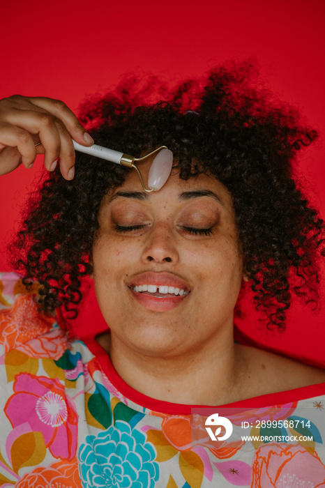 portrait of a plus size person using a face roller eyes closed