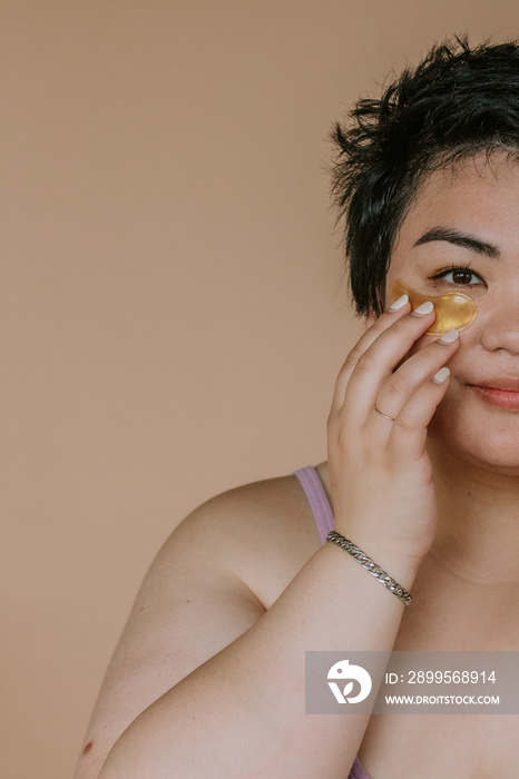 portrait of a plus size filipino woman applying under eye pad