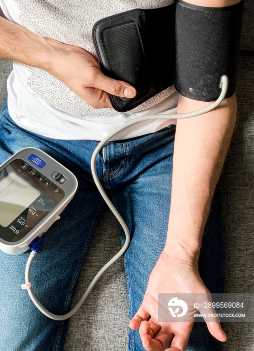 Man is checking blood pressure at home. Sitting on a gray sofa. Seasonal health issues. Hypertension or hypertension seasonal disorder and problems. Taking care of health, looking after yourself