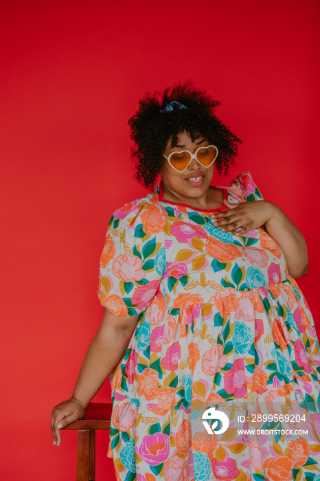 portrait of a plus size black person sitting on a stool wearing ad ress