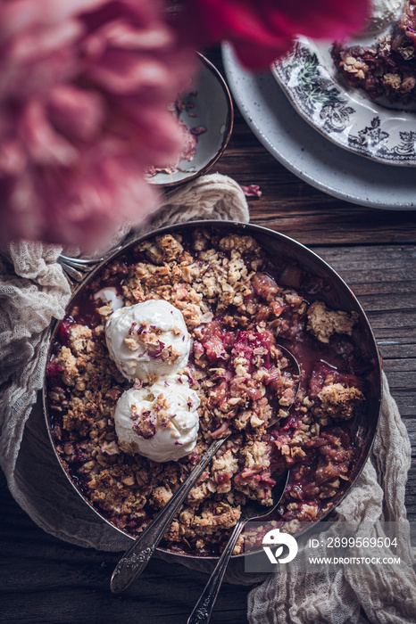Rose rhubarb cobbler with a scoop of vanilla ice cream. Rustic table setting, peony flowers