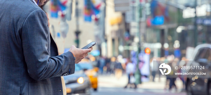 New York, Wall street. Young man in suit holding a smartphone