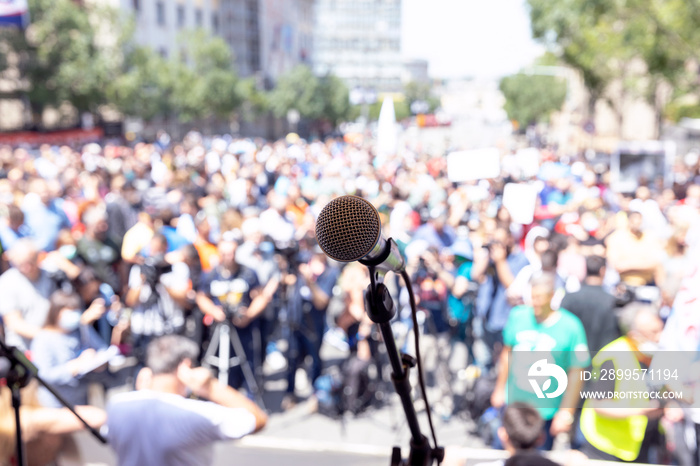 Focus on microphone, blurred group of people at mass protest against Covid-19 lockdown