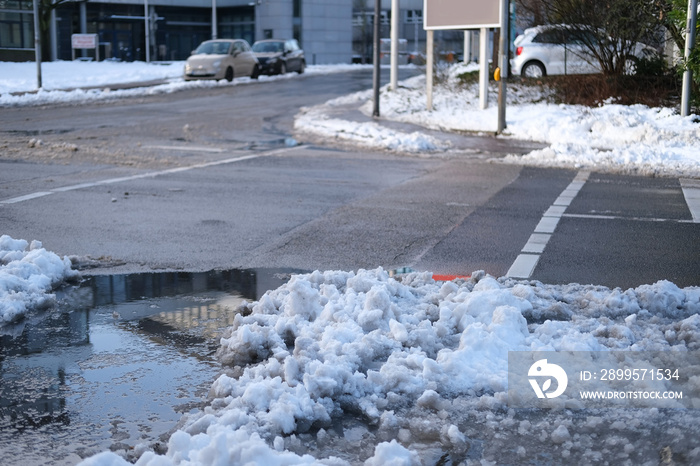 part of street in city, pavement after heavy snowfall, wet snow melts, puddles, slush and mud impede movement of pedestrians and vehicles, concept traffic safety, work of public utilities