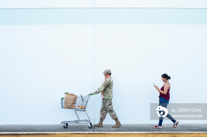 Soldier pushing a shopping cart holding girl with wife behind him