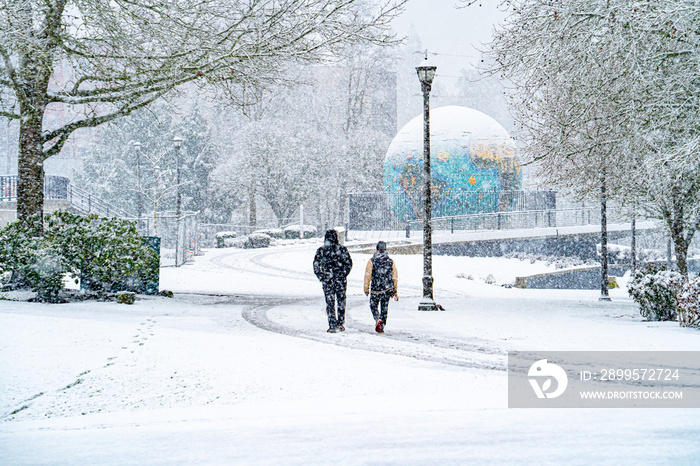 Duringa snow storm, two men walking in riverfront park with the eco-earth globe map in background, salem, Oregon