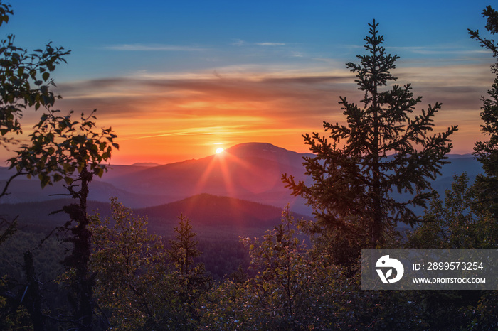 A rocky mountain range covered in the wild woods illuminated by the golden light of the setting sun. A natural Park reserve or hunting grounds. Recreational outdoor tourism