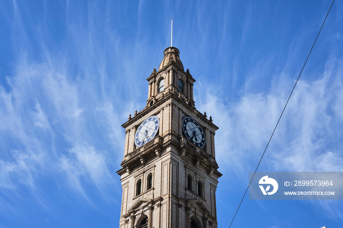 Historic Victorian style clock tower in Melbourne CBD with blue sky and white clouds