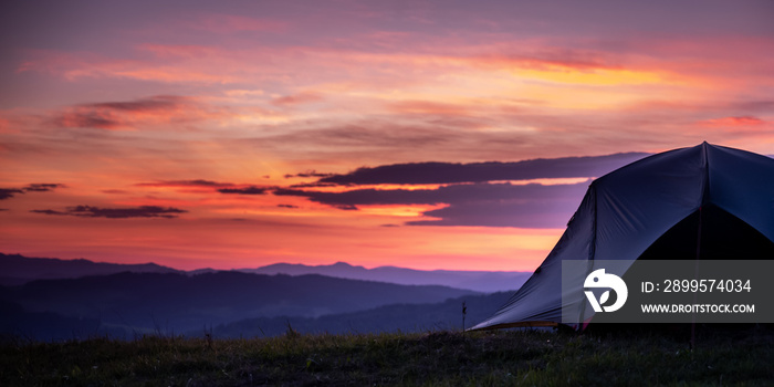 Tourist tent in the mountains under dramatic evening sky. Colorfull sunset in mountains. Camping travell concept. Traveler people enjoying the advanture alternative vacation