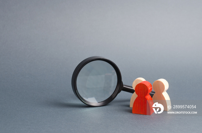 Three wooden human figure stands near a magnifying glass on a gray background. Search for vacancies and work. Human resources, management. The concept of the search for people and workers.