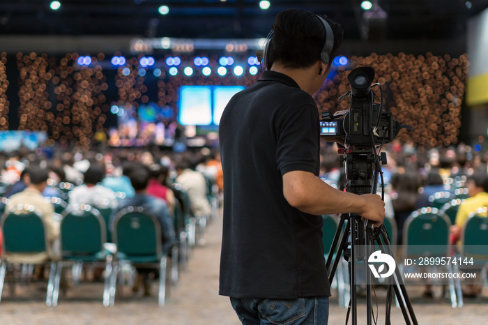 Rear side of Video Cameraman taking photograph to Abstract blurred photo of conference hall or seminar room in Exhibition Center background, event and seminar production equipment concept