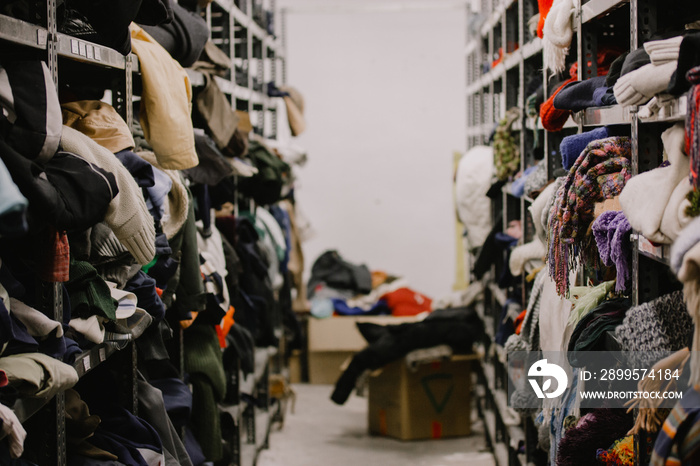 Humanitarian aid station, interior of industrial warehouse with used clothes for the poor, refugees, vulnerable people. Shelves, rows of clothes second hand. Stock clothing section collection.