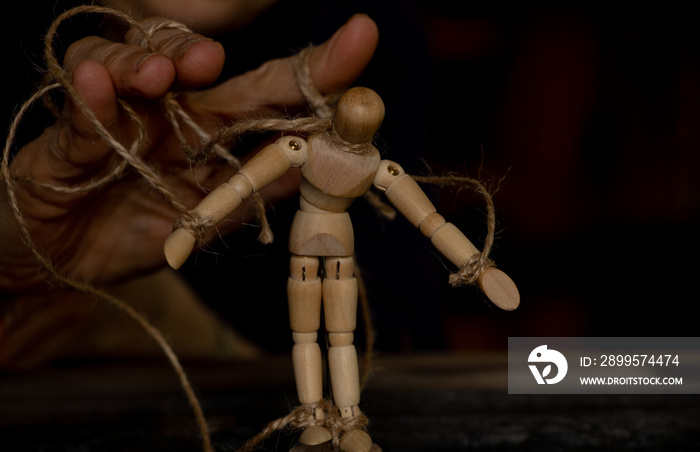 a wooden man on ropes tied to a man’s hand, manipulation of people and slavery, free will, power