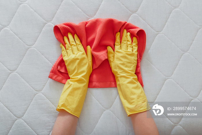 Employee cleans surface of mattress on bed with rag. Cleaning disinfection surfaces. Cleaning company person Hands in rubber gloves do Mattress chemical cleaning.