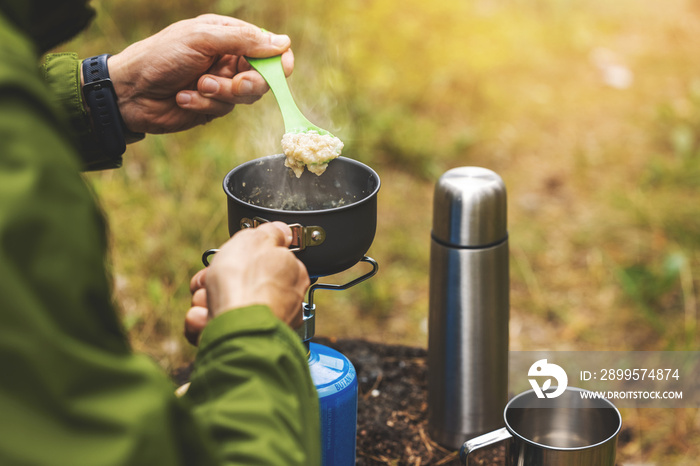 preparing oatmeal porridge outdoors on gas burner. camping cooking equipment