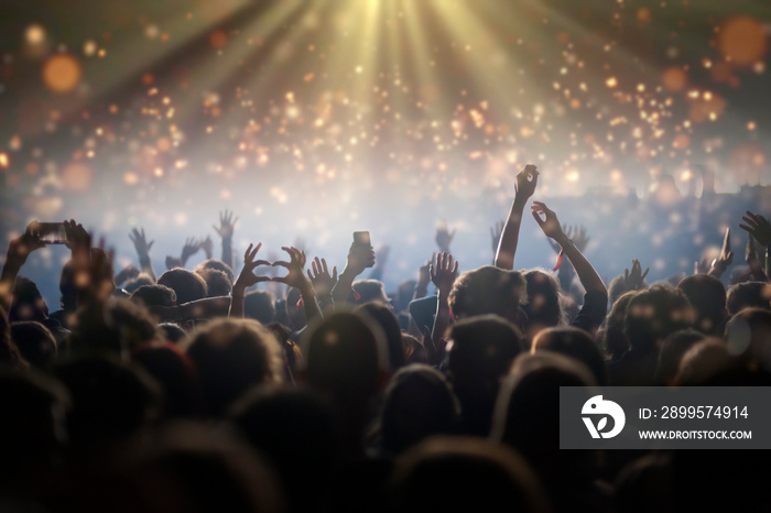 Stage lights and crowd of audience with hands raised at a music festival. Fans enjoying the party vibes.