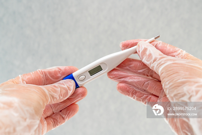 Female hands wearing in vinyl gloves holding a digital thermometer. Prevention of the spread of virus and epidemic, protective equipment concept