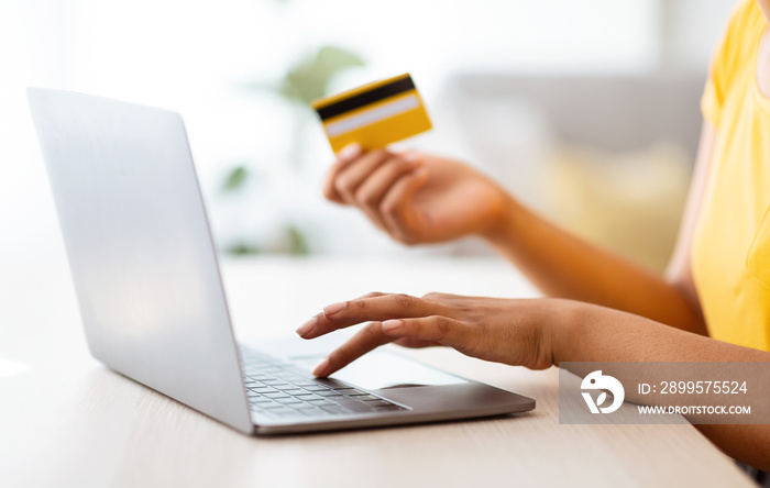 Black woman using laptop and credit card sitting at desk