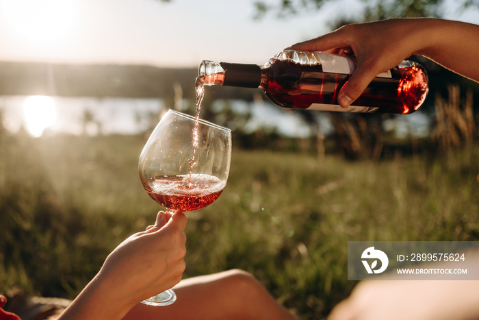 cropped view of couple pouring red wine on meadow, picnic summer day.