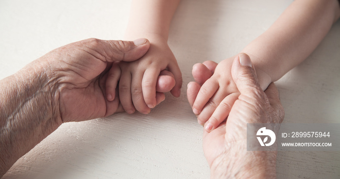 Elderly woman and a kid hands together.