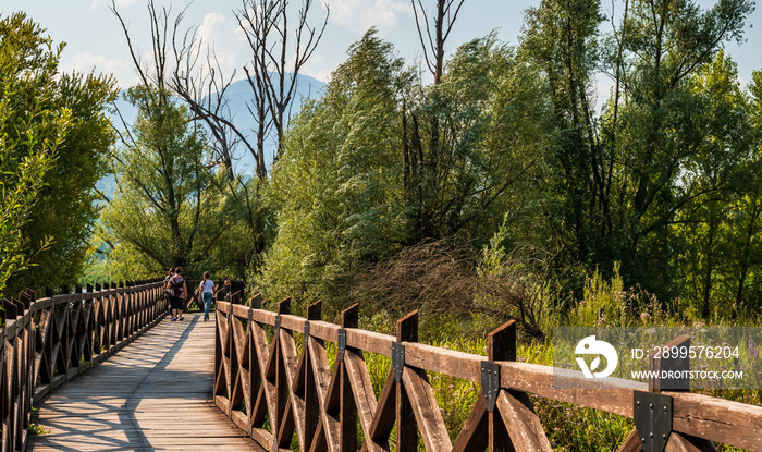 people walk on the wooden bridge through the Italian nature reserve Posta Fibreno amid the Italian Apennine mountains of the south-east Lazio region