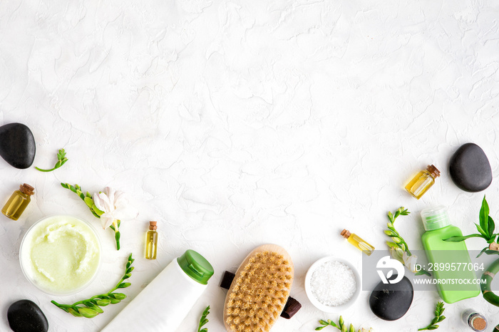 Top view of natural skincare and spa cosmetic products on white marble table, flat lay. Frame of cream, oil, sea bath salt, massage brush, bamboo and flower buds. Beauty flatlay concept