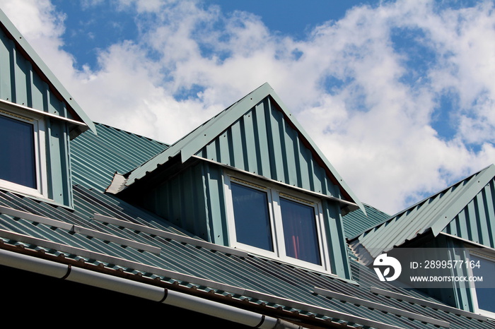 Roof windows on traditional mountain house with metal roof on warm cloudy blue sky background