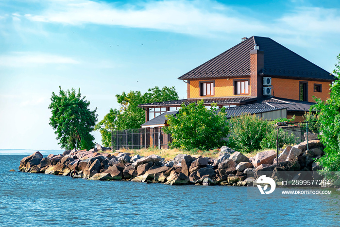 New modern brick house or cottage on the shores of the Kakhovsky reservoir in the Kherson region of Ukraine against the blue sky and water.