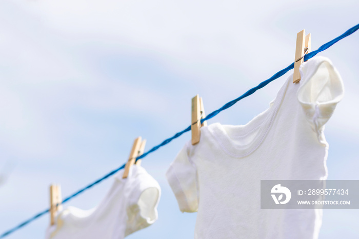 White baby clothes hanging on rope outdoors against blue sky