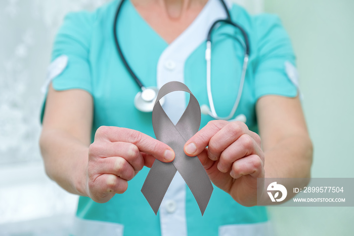 Doctor with stethoscope on his neck, shows a grey ribbon close-up in two hands. Parkinson’s disease or brain cancer awareness symbolic concept to help support the campaign against illness