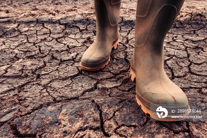 Farmer in rubber boots standing on dry soil ground