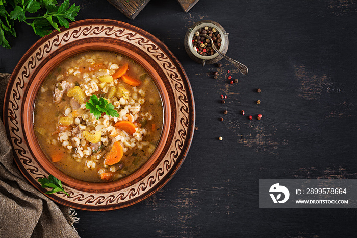 Barley soup with carrots, tomato, celery and meat on a dark background. Top view.