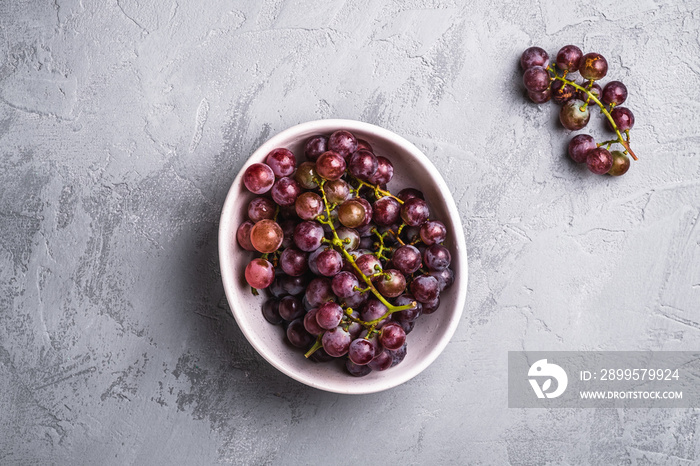 Fresh ripe grape berries in bowl on stone concrete background, top view