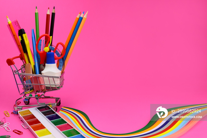 school or office supplies in supermarket trolley on pink background