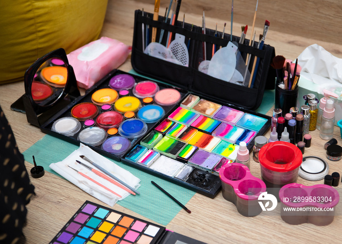 Colourful paint boxes and tubes with paints on a table. Paints and brushes for make-up, for painting on faces, face painting, face art. Abstract background and texture.