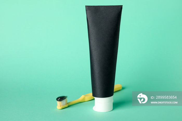 Tube of black tooth paste and brush on green background