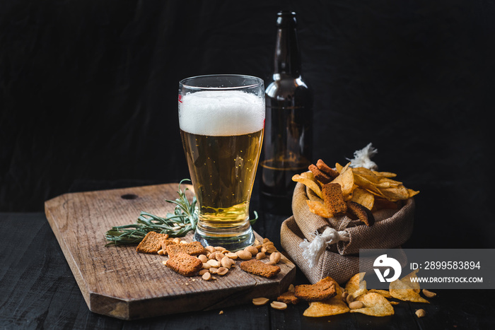 A glass of fresh beer with potatoe chips and peanuts on black background