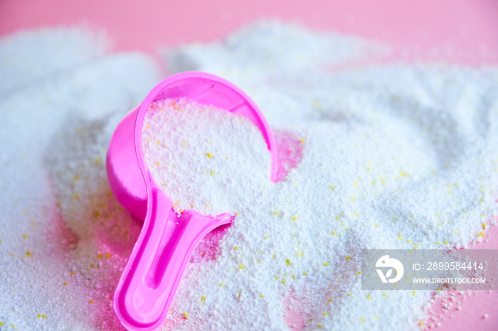 Measuring scoop with laundry powder on pink background