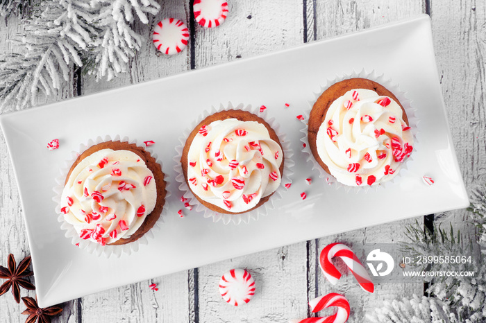 Christmas peppermint cupcakes with creamy frosting. Top view table scene against a white wood background.