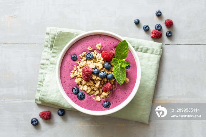 Smoothie bowl with granola and berries decorated with mint on wooden table. Top view.