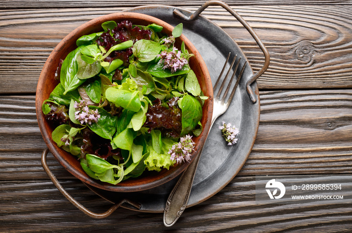 Top view at clay dish with green and violet lettuce, lamb’s lettuce salad with oregano flowers on vintage metal tray. Fork aside